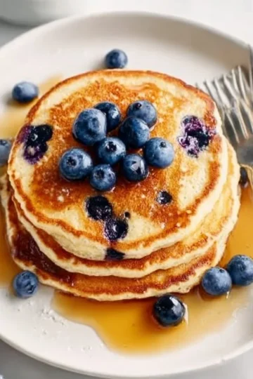 Fluffy blueberry pancakes topped with fresh berries and syrup on a plate.