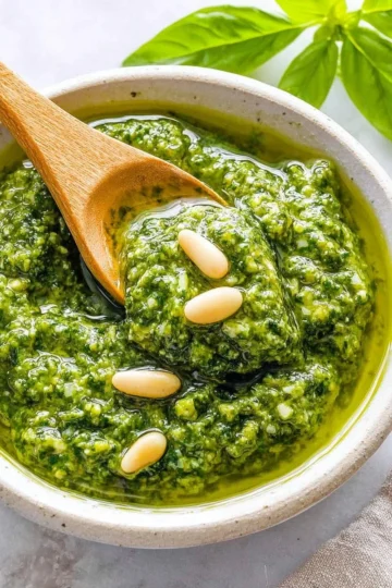 Basil pesto served in a bowl with fresh basil leaves and pine nuts