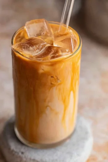 Delicious caramel iced coffee in a glass with ice cubes, topped with whipped cream.