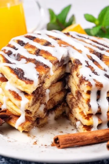 Stack of cinnamon roll pancakes drizzled with icing on a plate