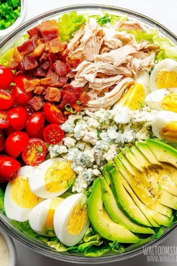 A colorful Cobb Salad with greens, bacon, chicken, and avocado arranged beautifully.