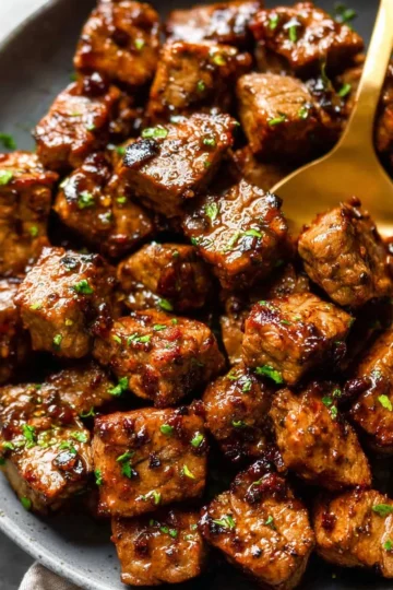 Delicious garlic butter steak bites served on a plate with herbs.