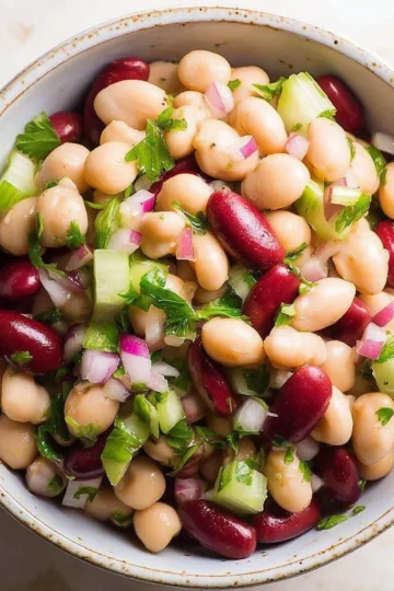 Three bean salad with colorful beans, vegetables, and dressing in a bowl.