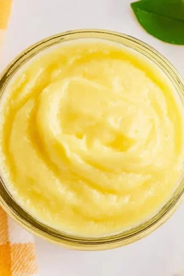 Classic lemon curd in a jar with fresh lemons and a spoon nearby.