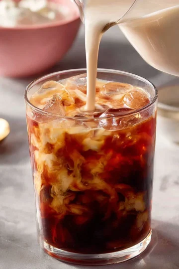 A glass of cold brew coffee with ice and coffee beans on a wooden table.
