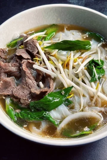 A bowl of homemade easy pho garnished with herbs and lime.
