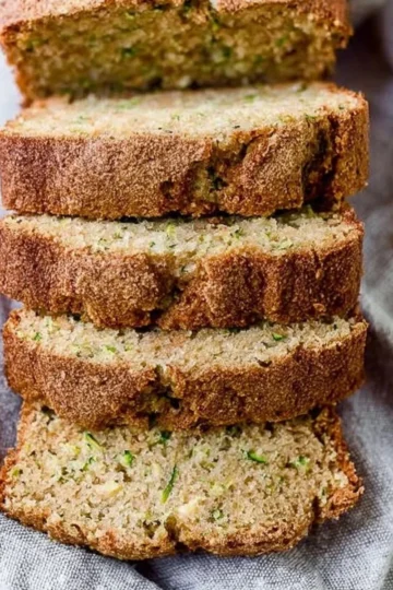 Freshly baked zucchini bread loaf with slices on a wooden cutting board.