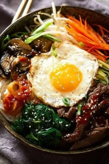 Bowl of colorful bibimbap with vegetables, rice, and egg for a delicious meal.